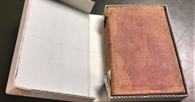 Cardboard archival box opened showing a rare book enclosed