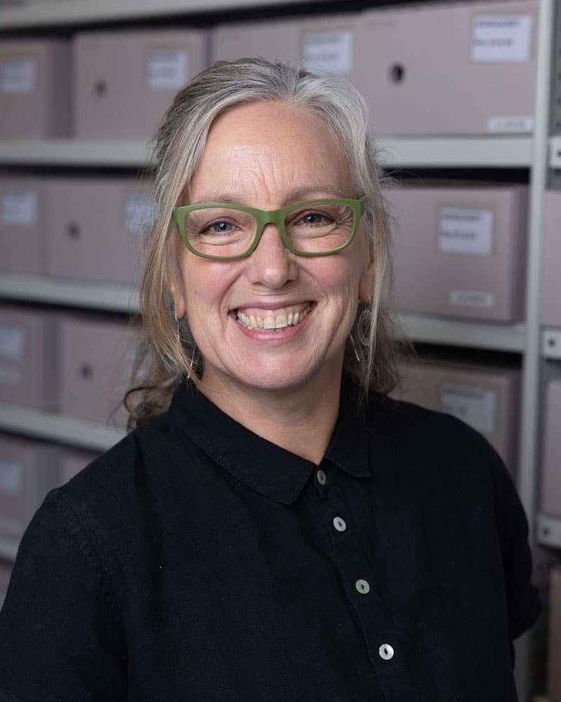 Head and shoulders portrait of Cathy Dodson. She is wearing green glasses, a black shirt, and is giving a warm smile.