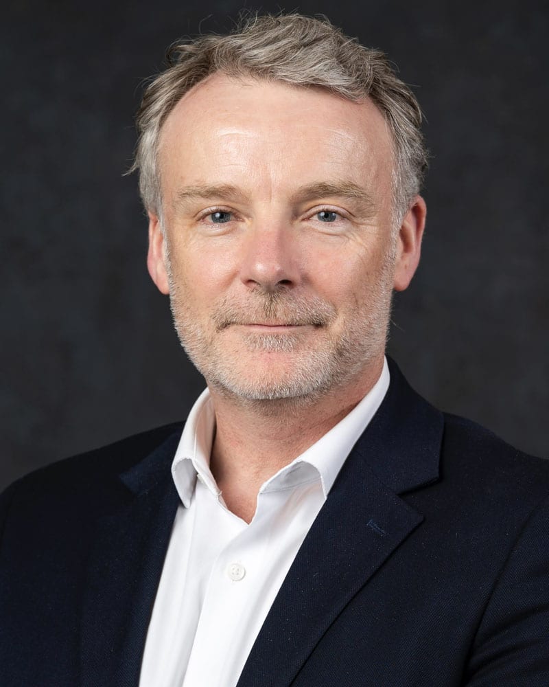 Professional headshot of Dr Steven Cooke. He is a middle-aged white man with greying hair and a bit of stubble. He is wearing a dark suit jacket and white shirt and looking into the camera giving a slight smile.
