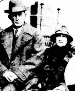 Black and white photo of a man and a woman sitting together. Both are wearing hats and coats.