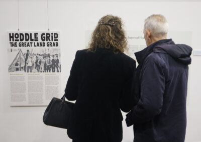 Two people are seen from the back, facing away from the camera as they admire the new exhibition display. The name of the exhibition is visible - "Hoddle Grid - the Great Land Grab"